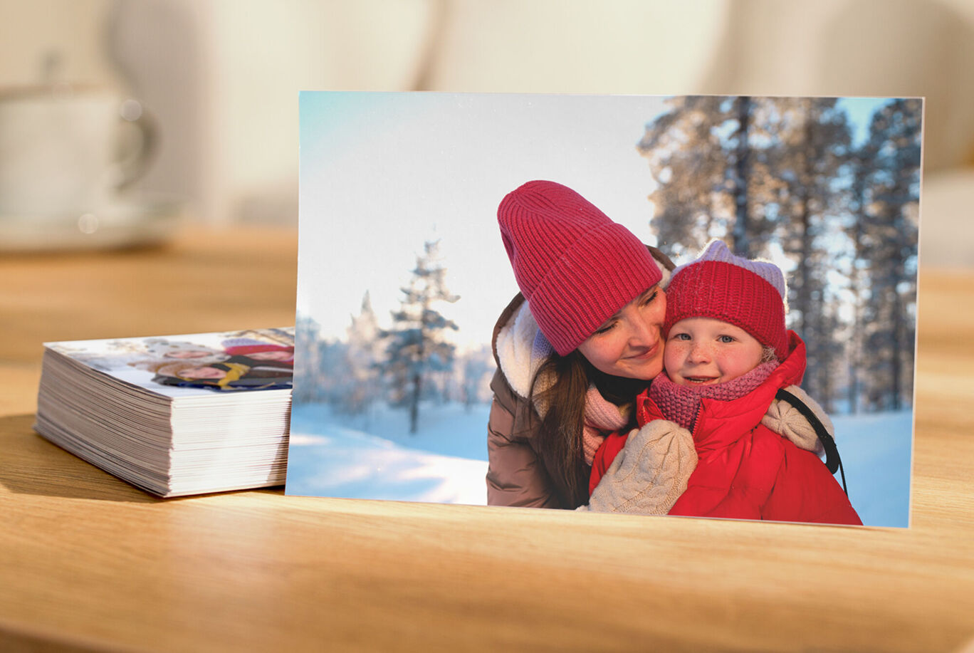 Eine lachende Mutter umarmt ihr Kind im Schnee; beide tragen Winterkleidung.