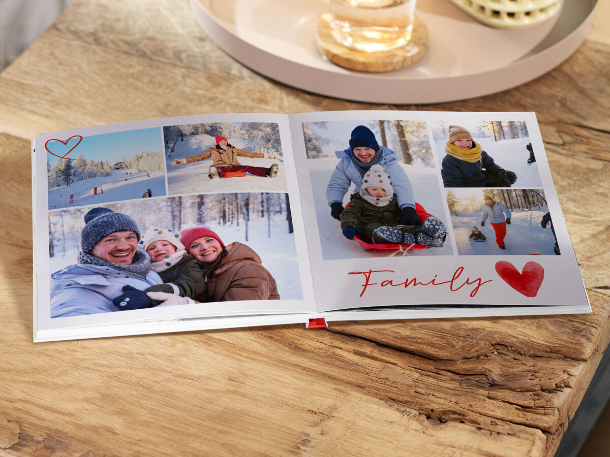 Aufgeschlagenes Fotobuch auf einem Holztisch mit winterlichen Familienfotos im Schnee; auf der rechten Seite steht „Family“.
