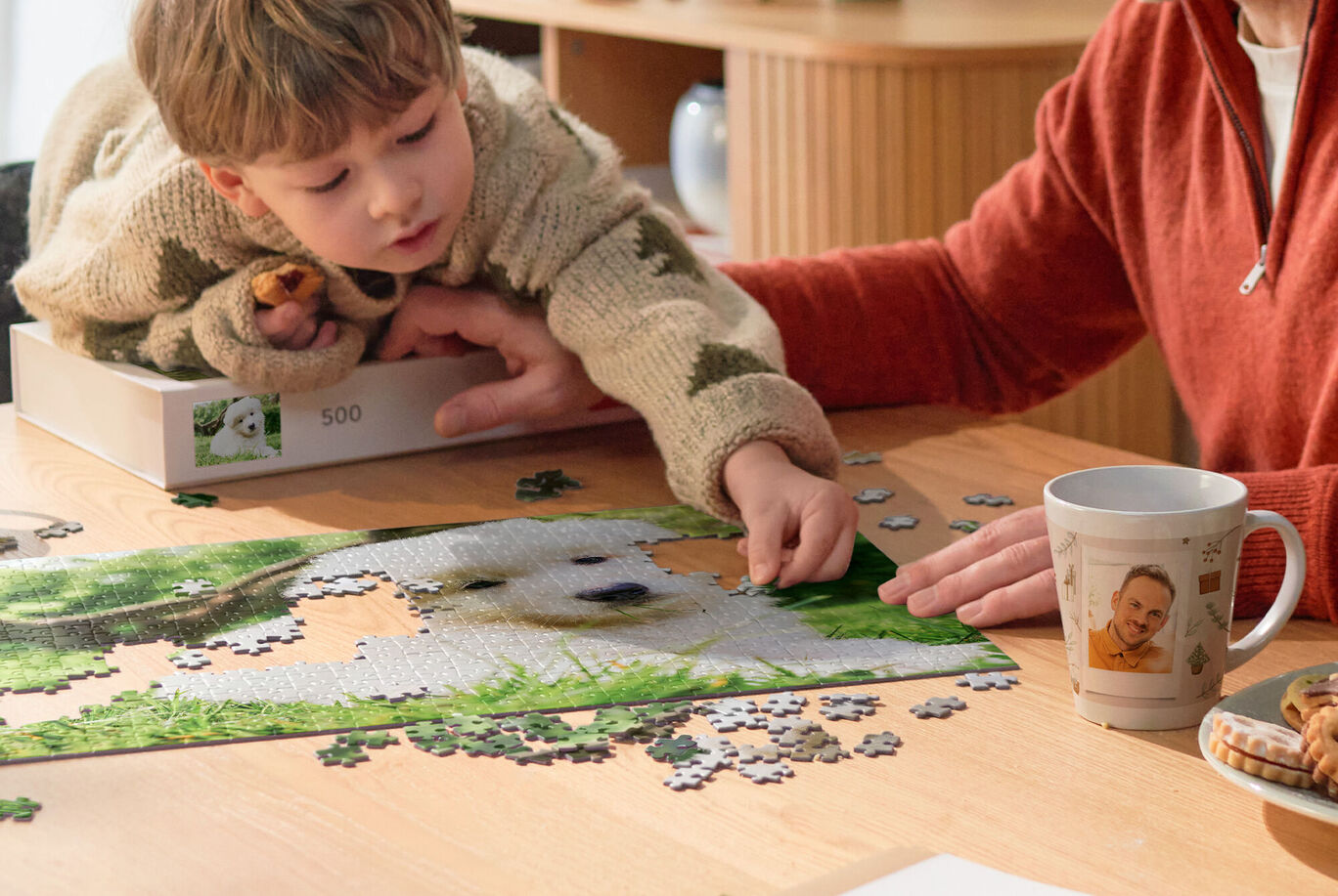 Kind und erwachsene Person legen gemeinsam ein CEWE Fotopuzzle mit Hundemotiv an einem Holztisch