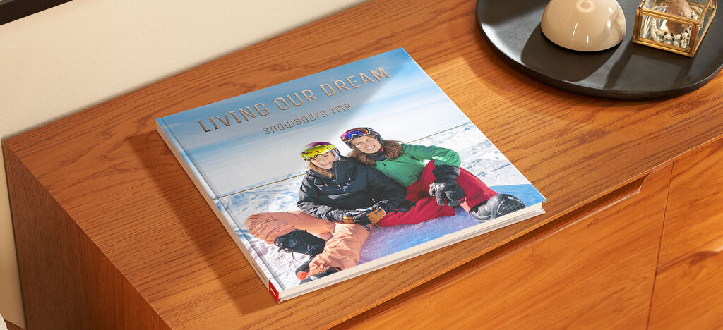 Ein offenes CEWE FOTOBUCH auf einem Holztisch, das zwei lächelnde Personen im Schnee zeigt