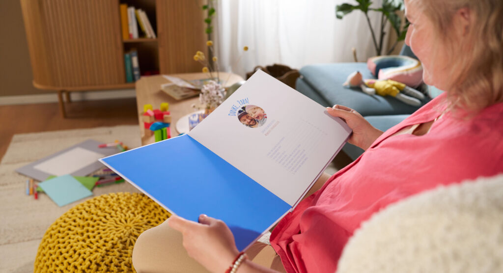 Eine Frau sitzt auf einem Sofa, in ihren Händen hält sie ein geöffnetes CEWE FOTBUCH.