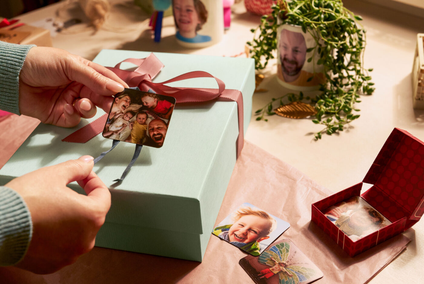 Eine Person befestigt zwei Magneten mit Fotomotiven als Anhänger an einem Geschenk.
